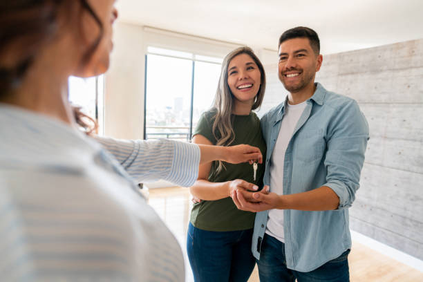 agent immobilier donnant les clés de leur nouvelle maison à un couple heureux - faire une passe photos et images de collection