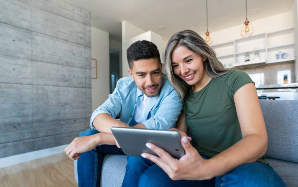 feliz pareja en casa viendo videos en una tableta - parejas latinas fotografías e imágenes de stock
