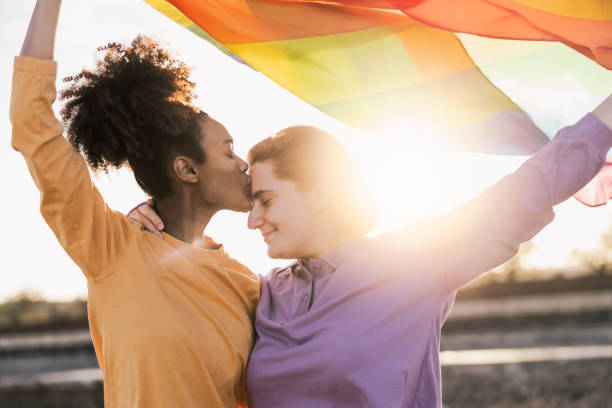 coppia lesbica felice che ha momenti romantici mentre tiene la bandiera arcobaleno all'aperto - concetto lgbt e amore - couple black american culture kissing foto e immagini stock