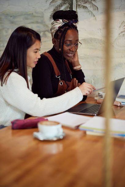 istock Two multicultural female students doing a school project on a laptop while drinking coffee in a cafeteria. 1393892440