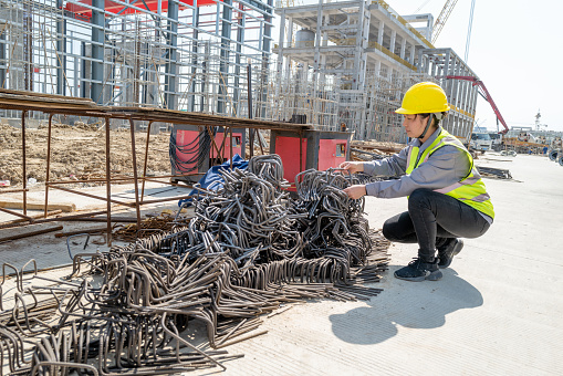 A female worker checks the quality of the formed steel bar on the construction site
