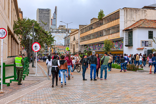 Bogota, Colombia - July 01, 2016: Carrera Septima once called Calle Real or Royal Street, at the point where it leads in to Plaza Bolivar in the Andean capital city of Bogota in Colombia, South America. This section of the Carrera has now been closed to vehicular traffic. It is now a 'pedestrian and cycles only' zone. Image shows local Colombian people going about their daily routine. To the left are the walls of the Supreme Court of the Country. In the far background, the tallest building in the Country, the BD Bacatá can be seen. The altitude at street level is 8,660 feet above mean sea level. Photo shot in the afternoon sunlight on a rather cloudy, overcast afternoon; horizontal format.