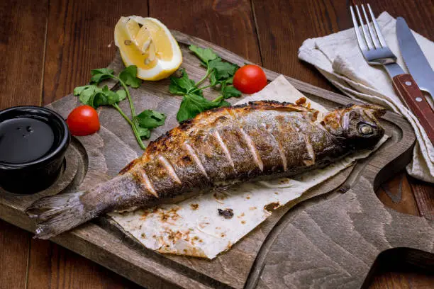 Photo of grilled trout on grill on a wooden board with lemon on wooden table