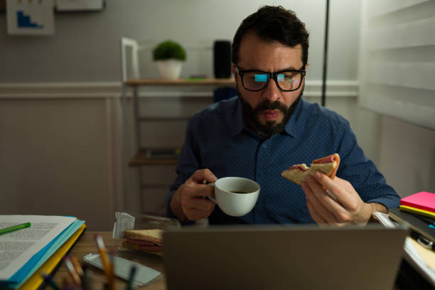 hungriger mann beim abendessen im büro - eating sandwich emotional stress food stock-fotos und bilder