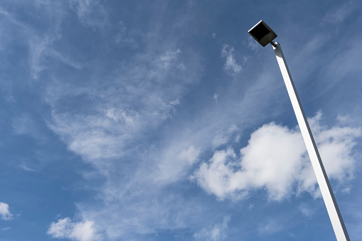 Looking up on an isolated light post in a cloudy blue sky.