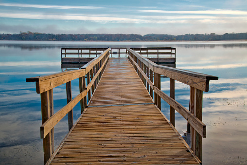 Dock extending out onto a tranquil Minnesota lake. The early evening clouds reflecting on the lake.