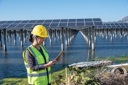 A female engineer works on a tablet computer at a seaside solar power plant