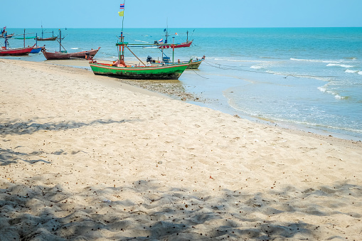 Beautiful view of the turquoise waves with the blue sky and white clouds and fisherman's boat on sandy on vacation in Hua Hin beach, Prachuap Khiri Khan Province, Thailand. Tropical colorful sand from the landscape sea. Summer vacation concept.