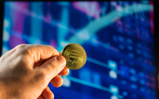 Man holding a golden Solana coin with the financial stock market graph in the background. Cryptocurrency coin. Financial market.