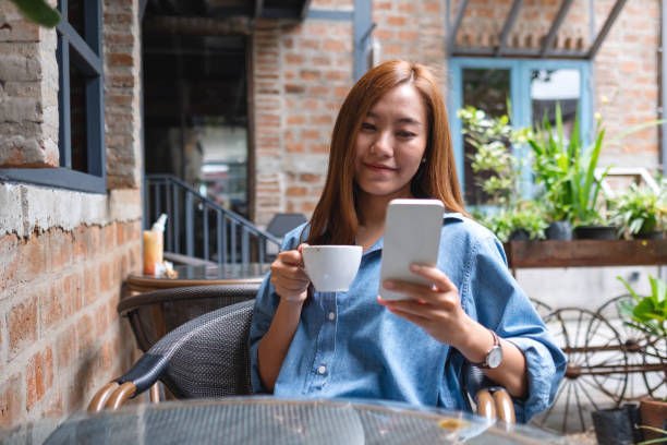 istock Portrait image of a young woman holding and using mobile phone while drinking coffee in the outdoors cafe 1393928263