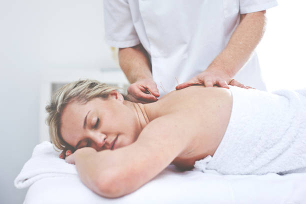 eine junge frau, die während einer akupunktursitzung nadeln in ihren rücken eingeführt bekommt. ein patient, der eine alternative therapie für die medizinische behandlung erhält - alternative medicine massaging spa treatment back stock-fotos und bilder