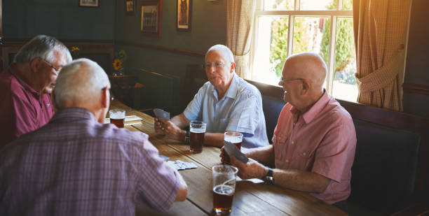 grupa starszych mężczyzn siedzących razem i grających w gry karciane w barze, wiążących się, starszych przyjaciół cieszących się grą w brydża w pubie - vehicle interior restaurant bar bar counter zdjęcia i obrazy z banku zdjęć