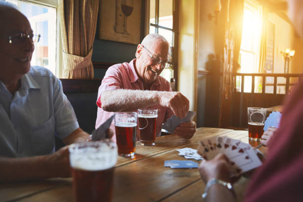 grupo de hombres mayores sentados juntos y jugando juegos de cartas en un bar, uniéndose, amigos mayores disfrutando de un juego de bridge en un pub - bridge juego de cartas fotografías e imágenes de stock