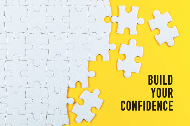 istock Build Your Confidence. Motivational text on white jigsaw puzzle with some missing pieces on yellow background. 1393937224