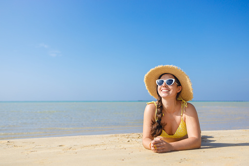 young smiling woman in straw hat and sunglasses lying on sand beach. Summer vacation concept