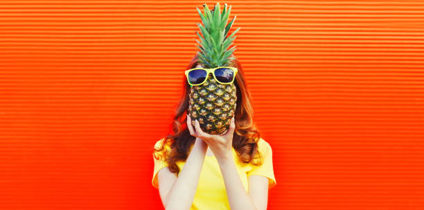 Fashion portrait woman covering her head and holding pineapple with sunglasses on red background stock photo