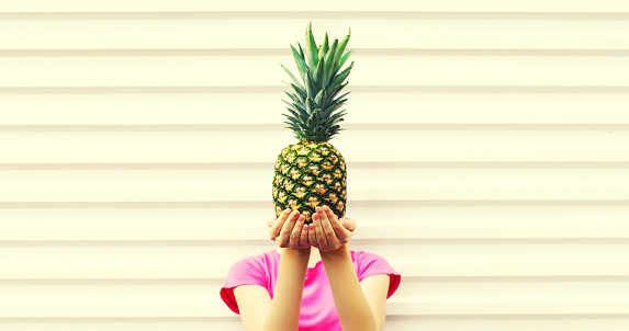 Fashion portrait woman covering her head and holding pineapple on white background, blank copy space for advertising text