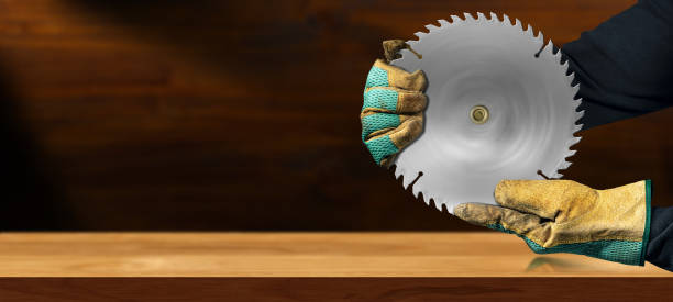 Gloved Hands Holding a Metal Circular Saw Blade on a Wooden Workbench Carpenter with protective work gloves holding a metal circular saw blade, in motion, above an empty wooden workbench with copy space. rotary blade stock pictures, royalty-free photos & images