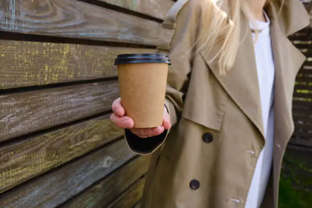 Photo of Paper cup with coffee in a woman's hand. Time to drink coffee in the city. Coffee to go. Enjoy the moment, take a break. Disposable paper cup close-up. Delicious hot drink. Empty space for text