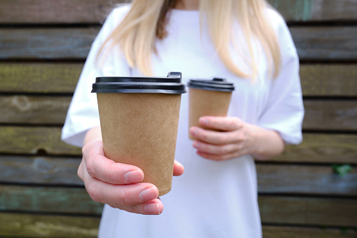Paper cup with coffee in a woman's hand. Time to drink coffee in the city. Coffee to go. Enjoy the moment, take a break. Disposable paper cup close-up. Delicious hot drink. Empty space for text