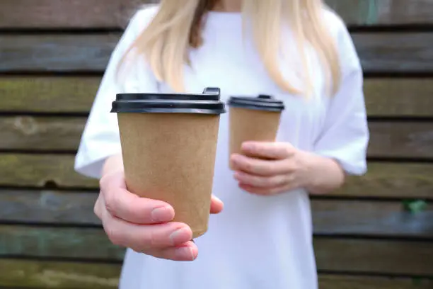 Photo of Paper cup with coffee in a woman's hand. Time to drink coffee in the city. Coffee to go. Enjoy the moment, take a break. Disposable paper cup close-up. Delicious hot drink. Empty space for text