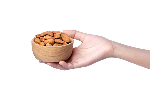 Woman hand holding wooden bowl with almond nuts isolated on white background.