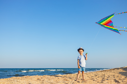little boy alone with flying colorful kite on sea beach. Summer fun on vacation