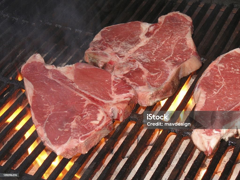 Steaks Cooking on the Grill - Raw Meat raw meat bone in steaks sitting over the flames of a charcoal grill cooking Barbecue - Meal Stock Photo