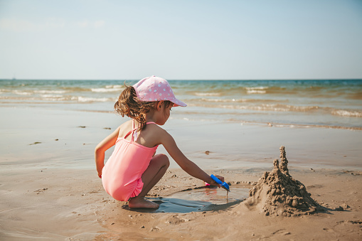 Cute little girl in a pink swimsuit playing with sand on the beach of a Baltic sea