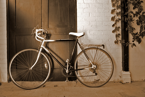 A racer bike leaning on a brick wall/door (sepia-toned).