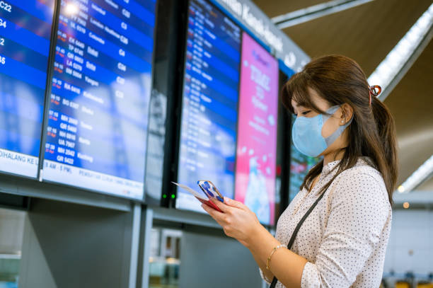 istock An Asian businesswoman wearing a facemask using smartphone checking her boarding schedule at the airport. Waiting in front arrival departure board. 1393965576