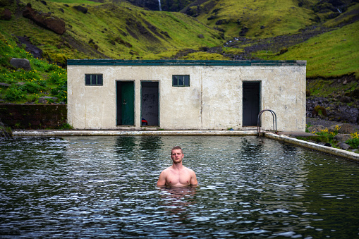 Young man in the Seljavallalaug geothermal pool located in south Iceland. This outdoor pool is free to use and is filled with naturally heated water.