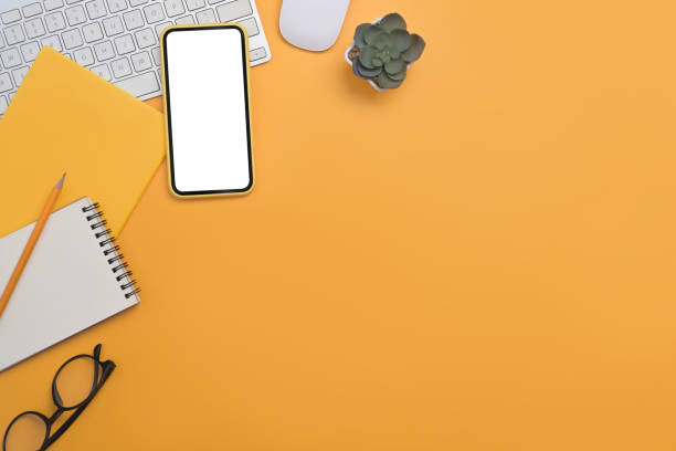 istock Above view mobile phone with blank screen, wireless keyboard and notebook on yellow background with copy space. 1393967099