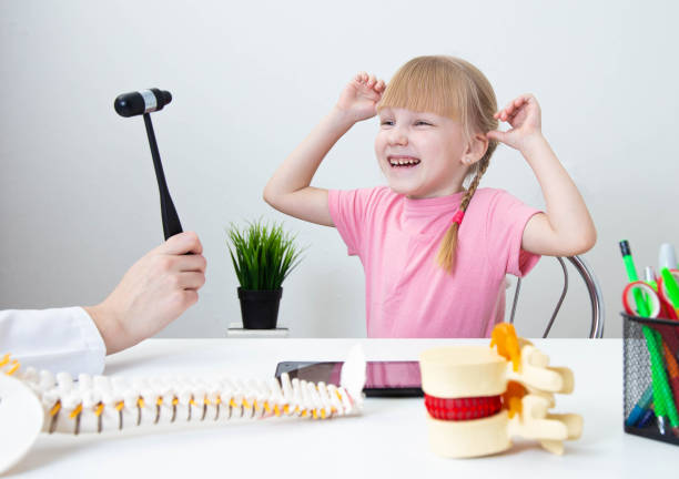 mała wesoła 5-letnia dziewczynka śmieje się w gabinecie neurologa i patrzy na młotek neurologiczny. badanie dzieci przez neurologa dziecięcego - neuropathologist zdjęcia i obrazy z banku zdjęć