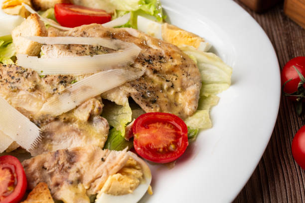 istock A Caesar salad with grilled chicken breasts, lettuce, croutons, eggs, cherry tomatoes, dressed with Parmesan cheese and sauce. On wooden background 1393970424