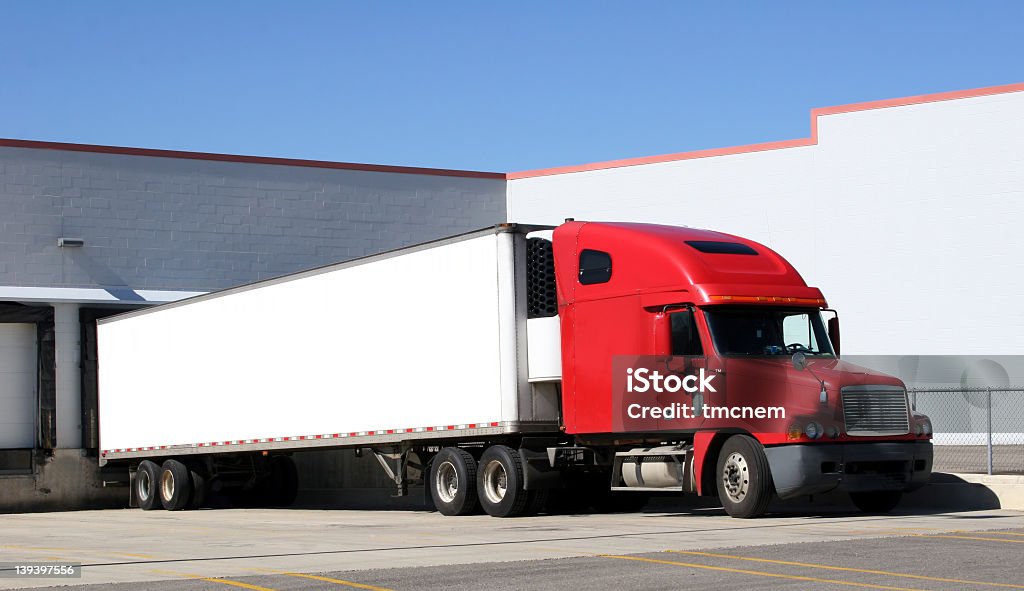 Red truck with trailer attached in parking lot Tractor trailer sitting at a loading dock.  Space for text on the trailer. Semi-Truck Stock Photo