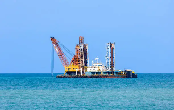 Dredging ship is bucketing mud in coastline to maintain water level for large vessel transportation while destroying marine habitat at shoreline