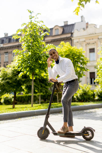istock Young African American using mobile phone while standing with electric scooter on a street 1393976439