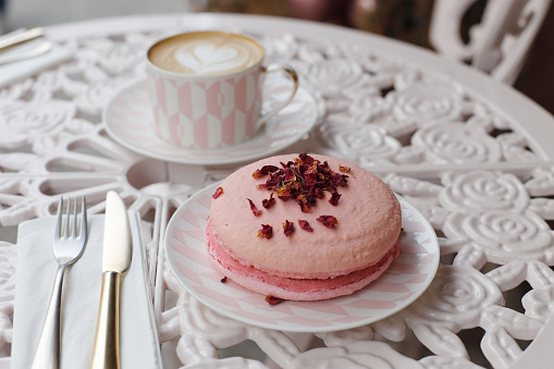 Cup of coffee and a big pink French macaroon on a cafe table.
