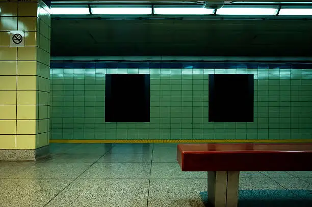 A vacant subway station with blank subway posters to use for design purposes.  Generic no smoking sign and bench in foreground.