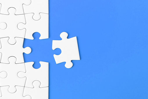 White jigsaw puzzle on blue background with copy space. Concept for: business strategy, teamwork and problem solving