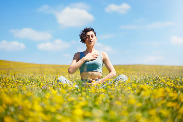 młoda kobieta medytująca i ćwicząca jogę na łące pełnej kolorowych polnych kwiatów i błękitnego nieba w słoneczny dzień. poszukiwanie duszy i duchowy relaks w przyrodzie - mantra zdjęcia i obrazy z banku zdjęć