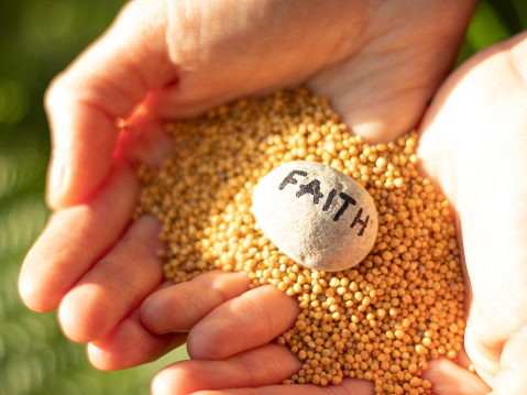 Woman hands holding mustard seeds and rock with handwritten word faith. Trust in God and Jesus Christ our Lord. Christian Bible concept. The gospel of Matthew 17:20 believe, hope and faith.