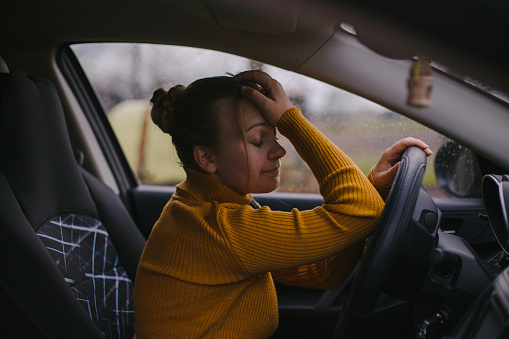 Young depressed womam sitting in car and holding her forehead.
