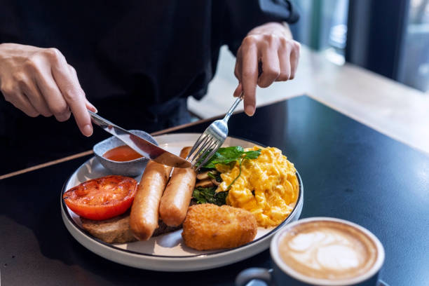 フォークとナイフを使って朝食を食べる女性 - sausage breakfast eggs fried egg ストックフォトと画像