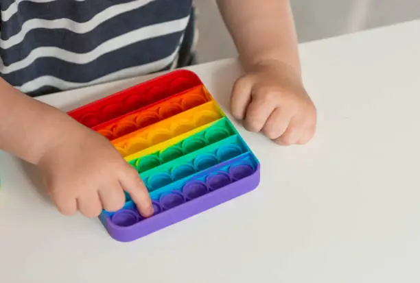 Photo of A child with a colorful pop it game. Anti-stress. A close-up shot of children's hands playing with the popular pop It fidget toy.