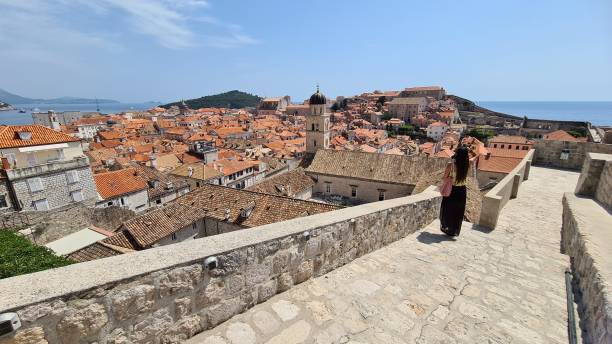 Woman enjoying the view of the roofs of the old town of Dubrovnik, Croatia. Old city of Dubrovnik. Sunny day in a coastal town, photographed by phone. dubrovnik walls stock pictures, royalty-free photos & images