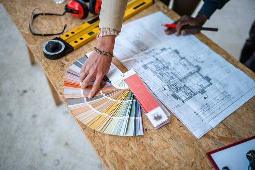 Close-up of a hand of an architect and interior designer pointing at a color swatch. There is a wide spectrum of colors and she is choosing grey.