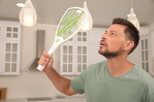 Man with electric fly swatter in kitchen. Insect killer