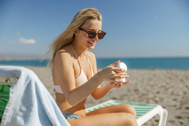 istock Smiling woman in sunglasses using body cream in jar while spending time on beach 1393994925